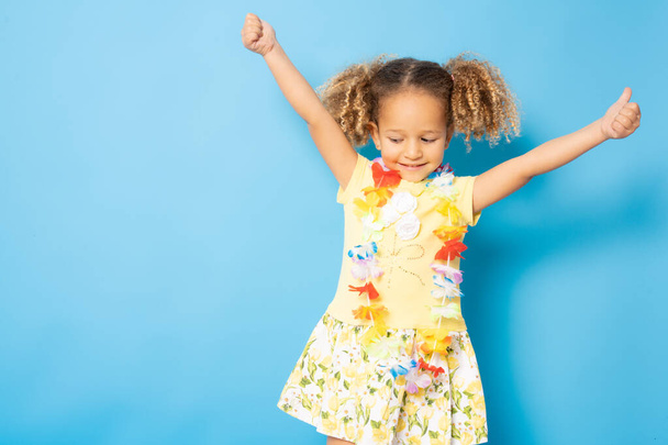 Happy little girl wearing Hawaiian necklace standing isolated over blue background. - Foto, afbeelding
