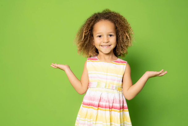 Smiling little girl with open arms standing isolated over green background. - Photo, Image