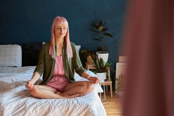 Tranquil person with bright hair and closed eyes meditates on large bed - Foto, Imagem