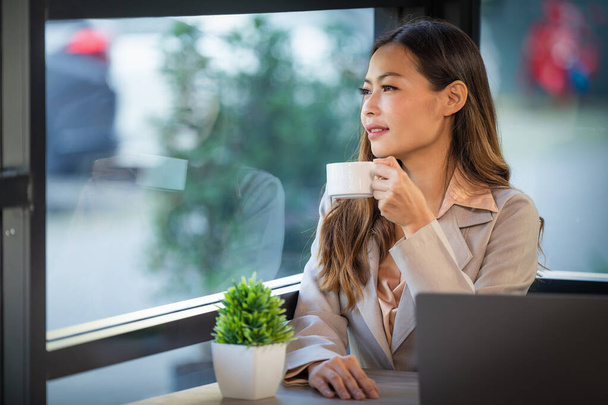 portrait of beautiful asian businesswoman sitting by window in coffee shop holding coffee cup with reflection on window - Фото, зображення