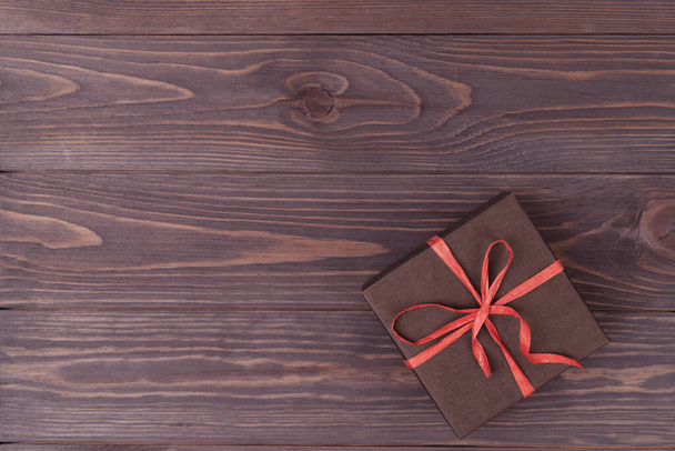 brown wooden background with a gift box packed in brown paper and tied with a red ribbon, lilac tinting - Фото, зображення
