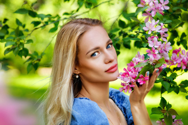 Gyönyörű lány kék ruhában egy virágzó rózsaszín almakertben. Lány és Sakura koncepció. Fiatal nő élvezi napsütéses nap a parkban alatt cseresznyevirág szezon egy szép tavaszi napon. Szépségportré. - Fotó, kép