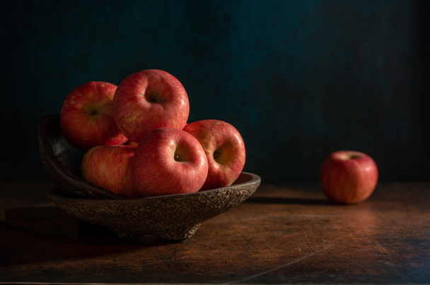 The apples on the plate look like oil paintings under the dim light on the wood grain table - Fotoğraf, Görsel