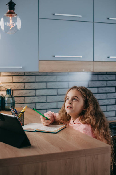 Kavkazská holčička studuje domácí úkoly během své online lekce doma s tabletem. Karanténa. Sebeizolace. On-line vzdělávání koncept. Covid-19. - Fotografie, Obrázek