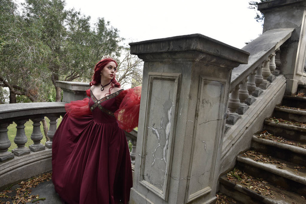  portrait of pretty  female model with red hair wearing glamorous gothic black lace ballgown.  Posing in a fairytale castle location with staircases  - Fotografie, Obrázek