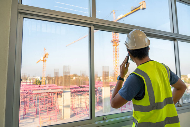 Architect or Engineer inspects the job site and works with a mobile phone, Crane on the construction site background. - Φωτογραφία, εικόνα