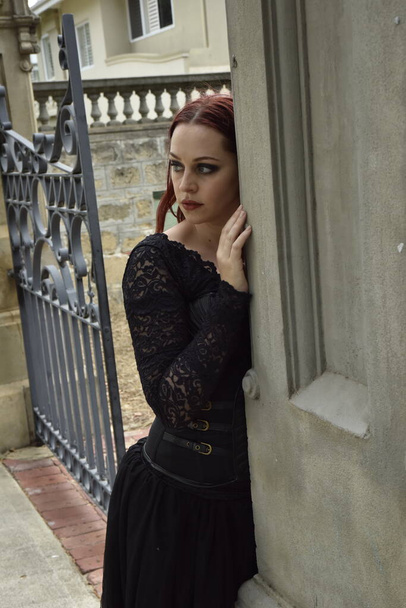  portrait of pretty  female model with red hair wearing glamorous gothic black lace ballgown.  Posing in a fairytale castle location with staircases  - Fotó, kép