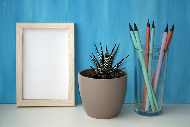 Mockup frame and plant in a pot by a blue wall. Pencils in a glass. Copy space. - Foto, Imagen
