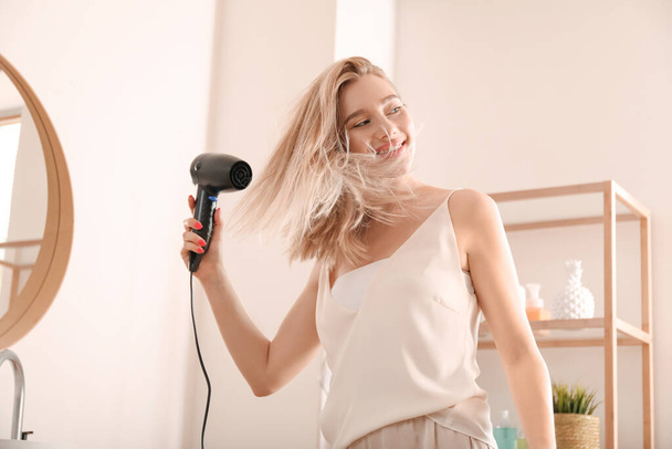 Pretty young woman blow drying her hair in bathroom - Photo, Image