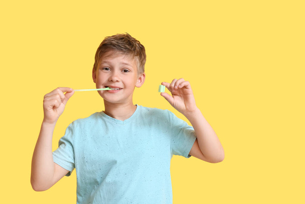Little boy in blue t-shirt with chewing gum on yellow background - Foto, Imagem