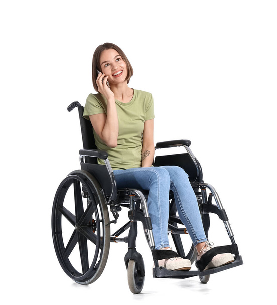 Young woman in wheelchair talking by phone on white background - Фото, изображение