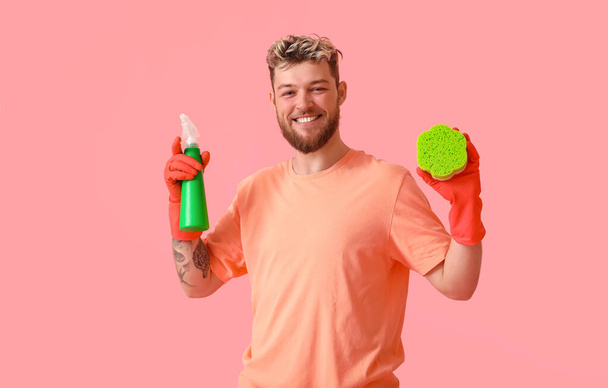 Handsome young man with cleaning sponge and detergent on pink background - Фото, изображение