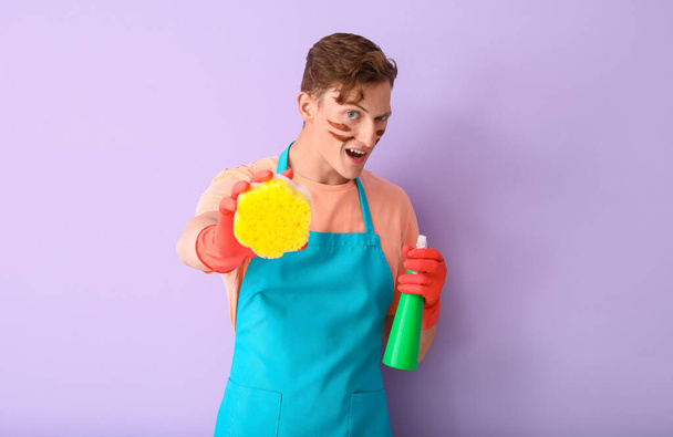 Hombre guapo con esponja limpiadora y detergente sobre fondo lila - Foto, Imagen