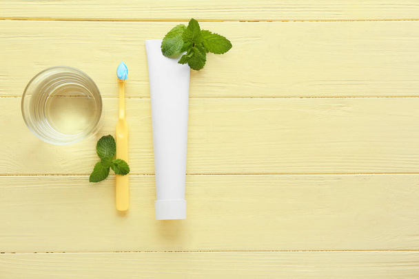 Tube with tooth paste, brush, mint and glass of water on color wooden background - Zdjęcie, obraz