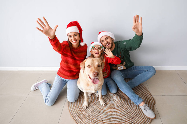 Happy family in Santa hats and cute Labrador dog near light wall - Фото, изображение
