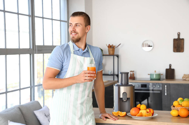 Young man with glass of fresh fruit juice near modern juicer in kitchen - Photo, Image