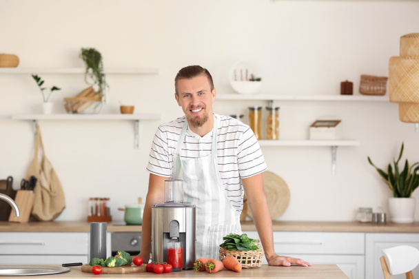 Молодий чоловік зі свіжими овочами та сучасним соковижималкою на кухні
 - Фото, зображення