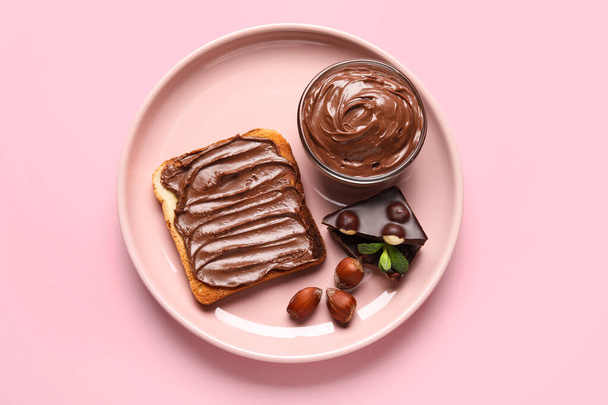 Plate of bread with chocolate paste and hazelnuts on pink background - Photo, Image
