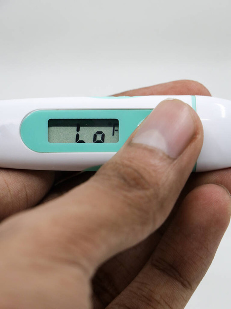 a closeup of the Low reading in a digital thermometer in the hands of a person isolated in a white background - Photo, Image