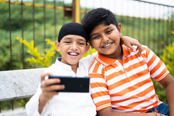 Kaksi onnellista monikansallista lasta, jotka ottavat selfien matkapuhelimeen puistossa ystävyyden, uskonnollisen monimuotoisuuden ja sosiaalisen harmonian konsepti - Valokuva, kuva