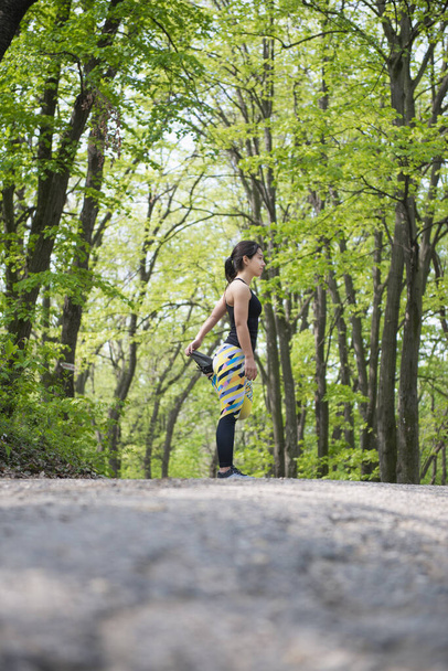 Atleta femenina estirando las piernas antes de un entrenamiento matutino en el bosque - Foto, Imagen