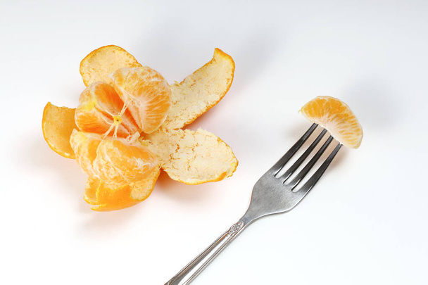 Disconnected from peel tangerine with juicy slices and fork, on a white background - Foto, afbeelding