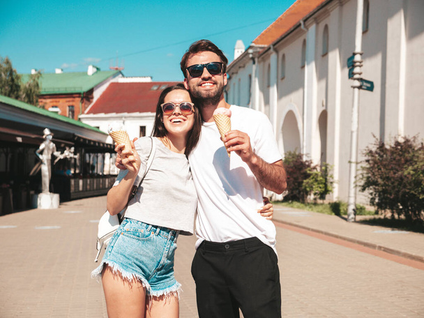 Smiling beautiful woman and her handsome boyfriend. Woman in casual summer clothes. Happy cheerful family. Couple posing on the street background in sunglasses. Eating tasty ice cream in waffles cone - Photo, Image