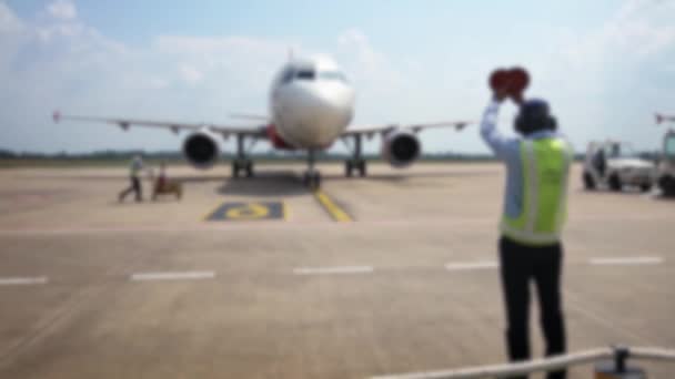 Снимок снятый работником аэропорта, подающим сигнал пилоту самолета на взлетно-посадочной полосе. Прибытие самолета в международный аэропорт. Коммерческие пассажирские недорогие самолеты. Размытый фон в сцене - Кадры, видео