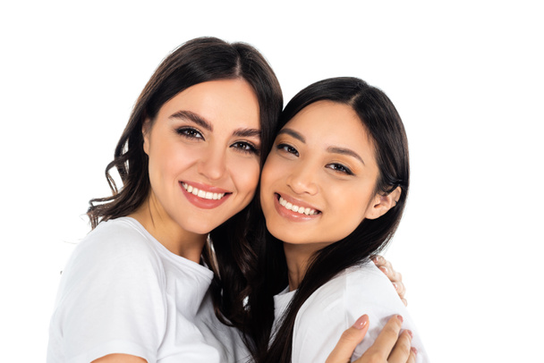 happy brunette woman embracing and looking at camera with asian friend isolated on white - Foto, Imagem