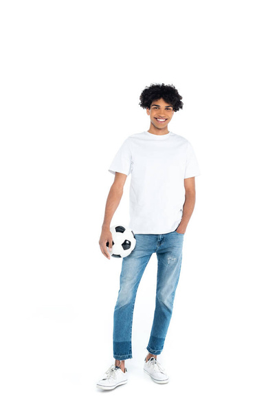 onnellinen afrikkalainen amerikkalainen mies seisoo käsi taskussa pitäen jalkapalloa valkoisella - Valokuva, kuva