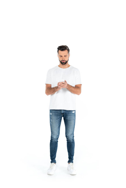 full length view of man in jeans chatting on smartphone on white - Foto, Imagem