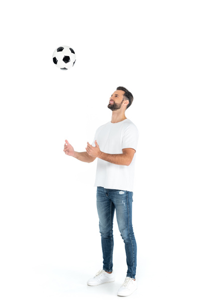 full length view of cheerful man in jeans playing with soccer ball on white - Fotó, kép