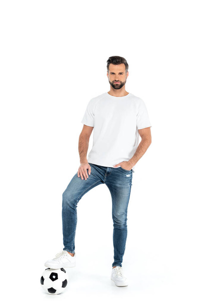 full length view of man stepping on soccer ball while standing with hand in pocket of jeans isolated on white - Fotografie, Obrázek