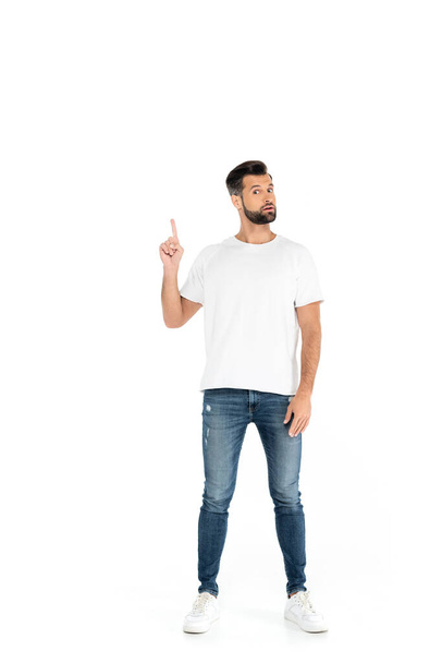 full length view of bearded man in t-shirt and jeans pointing with finger on white - Fotó, kép