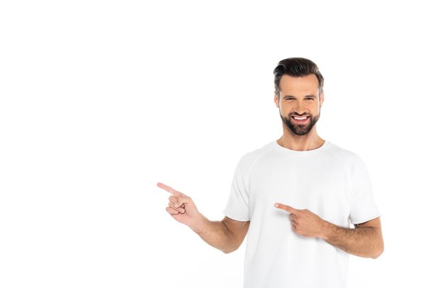 happy man in t-shirt pointing with fingers while looking at camera isolated on white - Foto, afbeelding