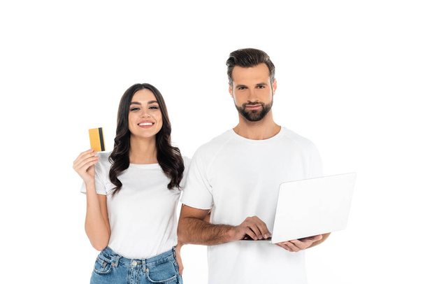 glückliche Frau hält Kreditkarte in der Nähe Mann mit Laptop isoliert auf weiß - Foto, Bild