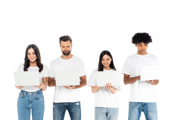 smiling multiethnic freelancers in t-shirts and jeans using laptops isolated on white - Zdjęcie, obraz