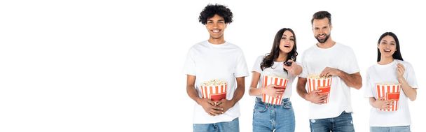 joyful multiethnic friends eating popcorn while watching movie isolated on white, banner - Foto, afbeelding