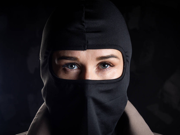 Portrait of a girl in a black balaclava and beige coat. Shot in the studio on a dark background. - Photo, Image
