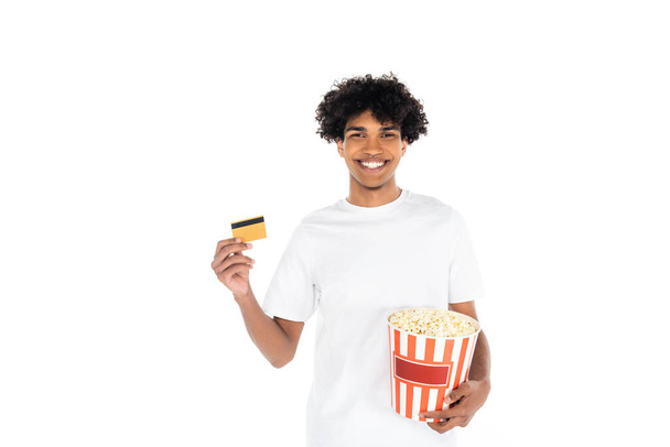 tevreden Afro-Amerikaanse man met emmer popcorn en creditcard geïsoleerd op wit - Foto, afbeelding