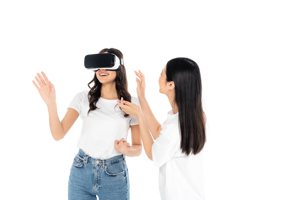 cheerful woman gaming in vr headset near asian friend isolated on white - 写真・画像