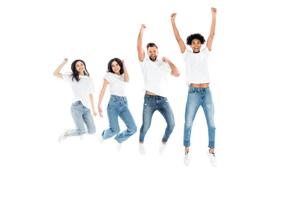 full length view of excited multicultural friends in jeans showing win gesture while levitating isolated on white - Foto, afbeelding