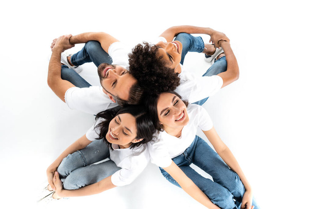 top view of happy multiethnic friends sitting back to back on white - Photo, image