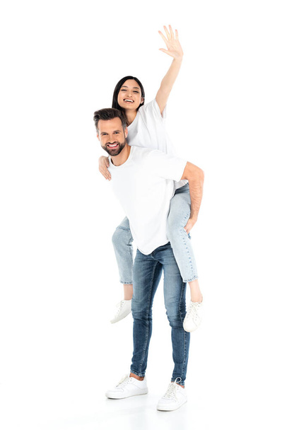 man in jeans piggybacking excited asian woman waving hand on white - Foto, immagini