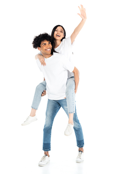 smiling african american man piggybacking excited asian woman waving hand on white - Photo, Image
