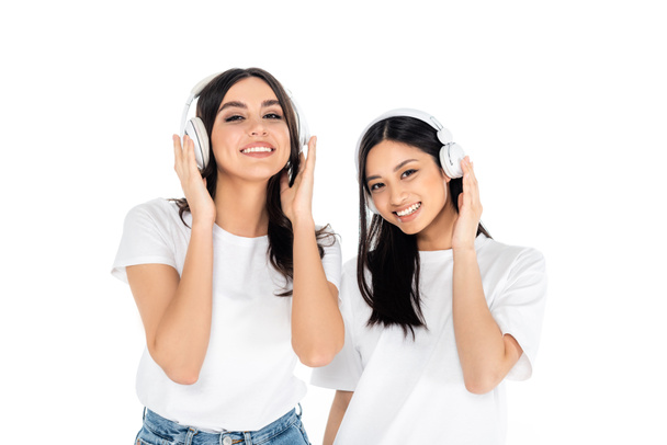 brunetky mezirasové ženy s úsměvem na kameru při poslechu hudby ve sluchátkách izolovaných na bílém - Fotografie, Obrázek