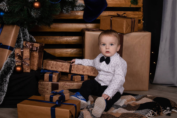 little toddler blonde boy near christmas tree in dark loft room with blue decoration. happy new year - Foto, afbeelding