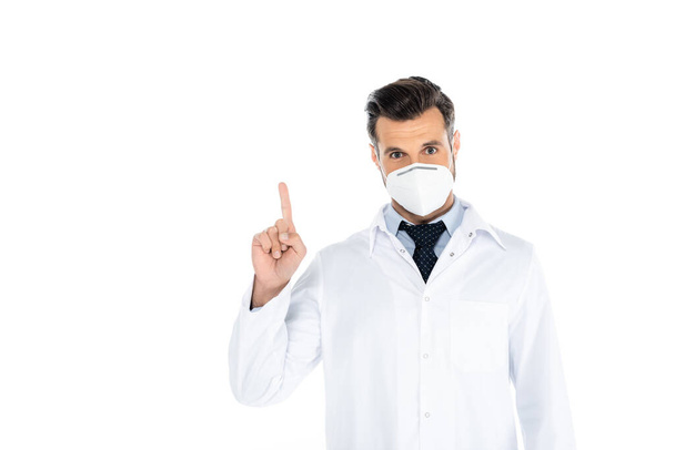 doctor in white coat and medical mask looking at camera and pointing with finger on white - Foto, Imagem