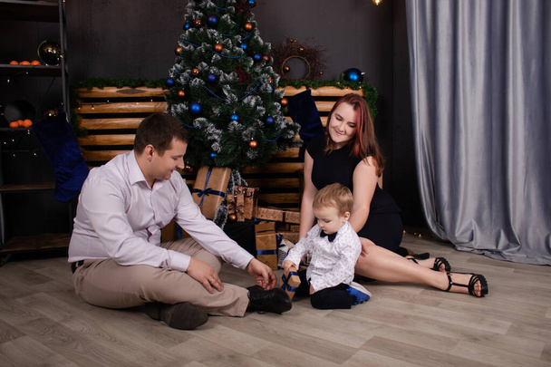 father and mother holds their little blonde son and pose near the Christmas tree. Concept of family holiday. Young parents and baby boy have fun and hugs together in interior decorated for New year - Valokuva, kuva