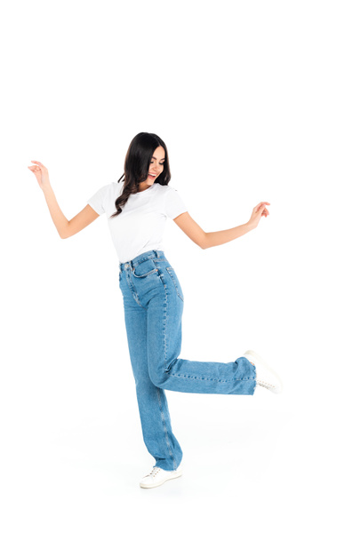 full length view of joyful brunette woman in jeans dancing on white - Fotografie, Obrázek